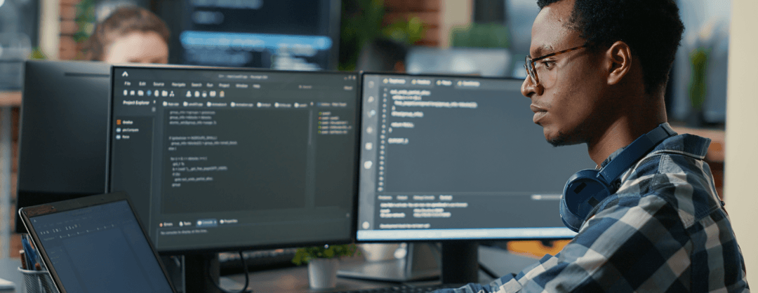 Software developer thinking while typing on a laptop at a desk with multiple screens